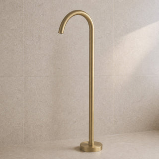 Brushed brass freestanding bathtub faucet against a beige tiled wall