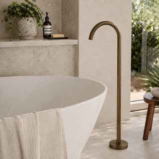 antique brass bath floor tap in a modern bathroom with free standing bath and beige tiles