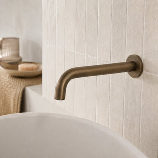 antique brass bathroom wall tap inn a modern bathroom with a free standing bath and beige tiles