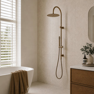 Antique brass gooseneck rain shower head and hose set in a modern bathroom with beige tiles and a free standing bath