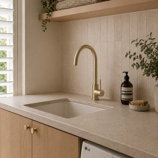 Modern laundry with brushed brass faucet tap, sink, and light coloured cabinets.