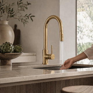Gold kitchen tap in a modern organic kitchen setting with a person washing hands.